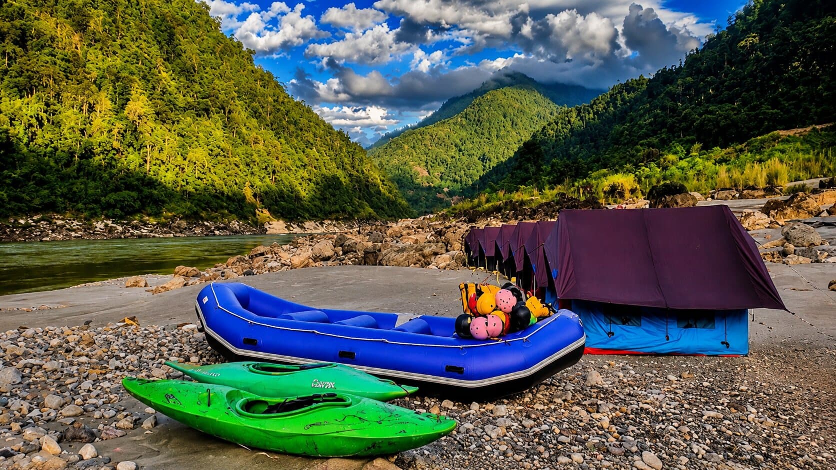 A rafting camp on the banks of the Siang — rafts, kayaks and riverside tents beneath the forested hills of Arunachal Pradesh